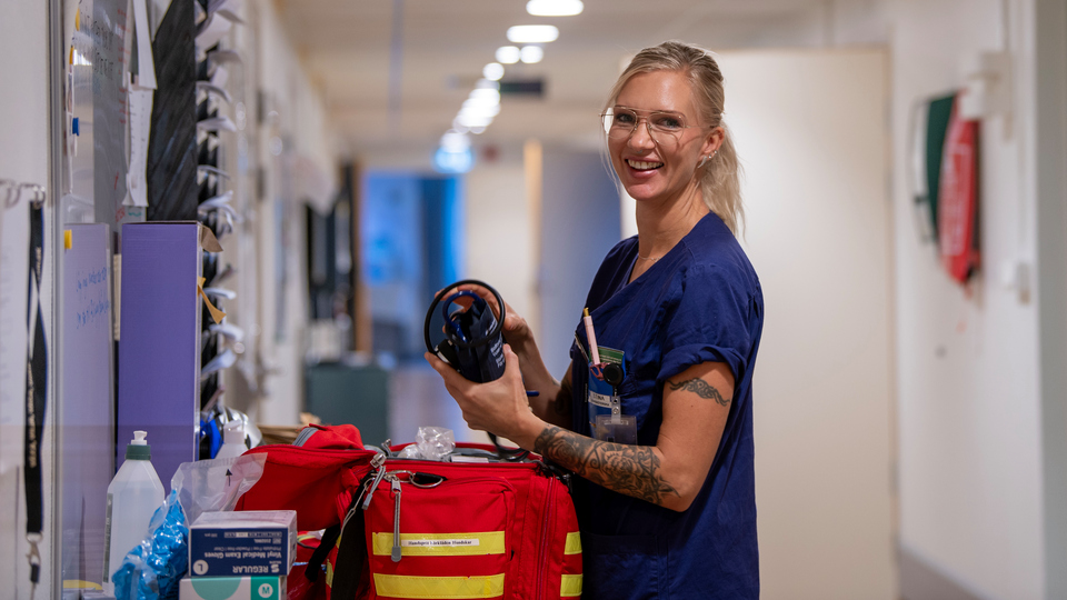 En kvinna i blå vårdklädsel står vid en Akutvårdsväska.