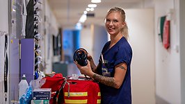 En kvinna i blå vårdklädsel står vid en Akutvårdsväska.